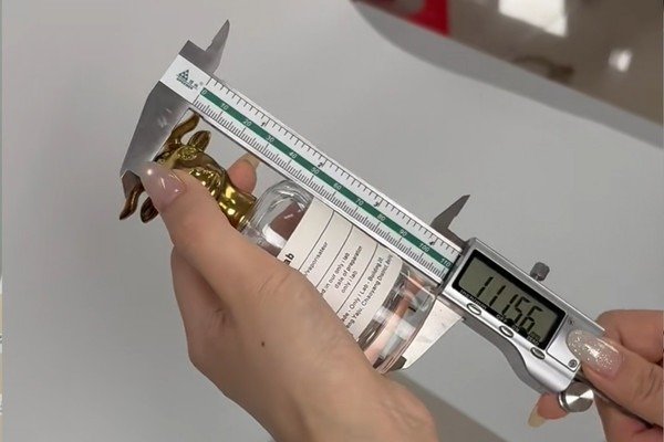 Image: hand measuring cosmetic bottle height, width, depth, and cap size cosmetic product measurements for packaging quotation